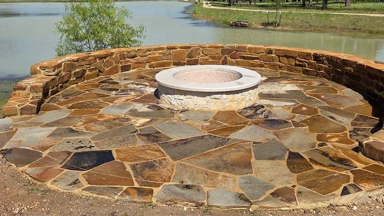 Round flagstone patio with a curved stone seat wall and a round fire pit, on the edge of a lake, built by GZ Masonry