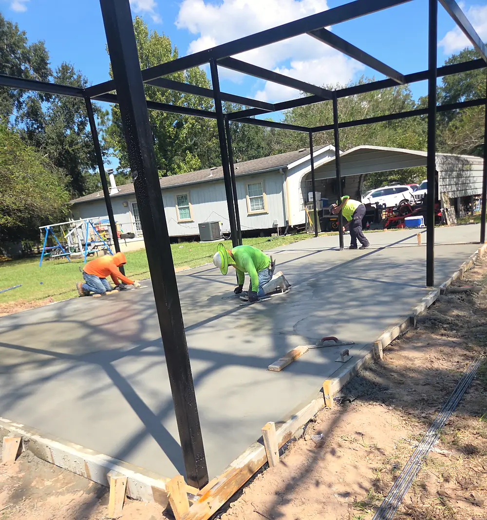 Crew finishing a fresh concrete slab under a new steel frame